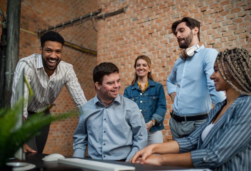 A happy down syndrome man with business colleagues in office, social inclusion and cooperation concept.