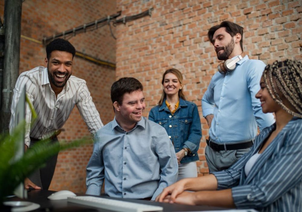 A happy down syndrome man with business colleagues in office, social inclusion and cooperation concept.